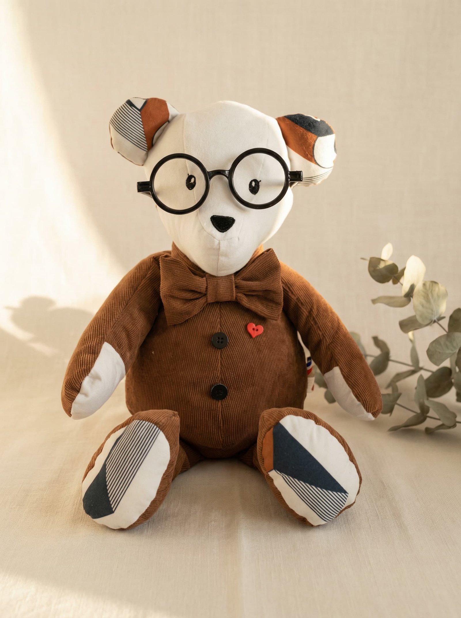 Ours cousu d'une veste en velours côtelé marron, nœud papillon, lunettes rondes, cœur-bouton rouge sur le torse